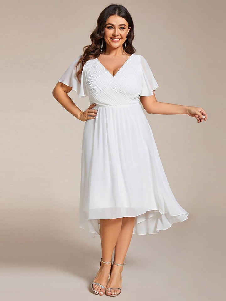 Witte chiffon jurk gedragen door een model met curves, hand op de heup, met asymmetrische zoom en gouden sandalen. 73