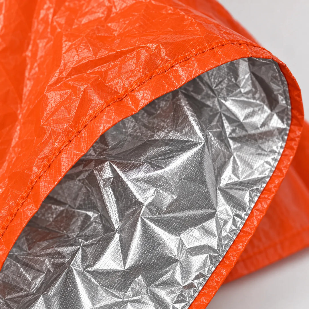 Close-up van de zoom van de oranje poncho met naad en de zilverkleurige, gekreukelde binnenlaag die warmte moet vasthouden. 5