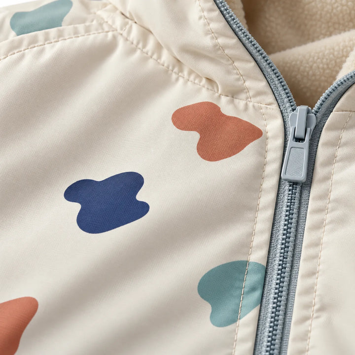 Close-up van de jas met kleurrijke vlekkenprint, grijsblauwe rits en zachte beige fleecevoering bij de kraag. 6