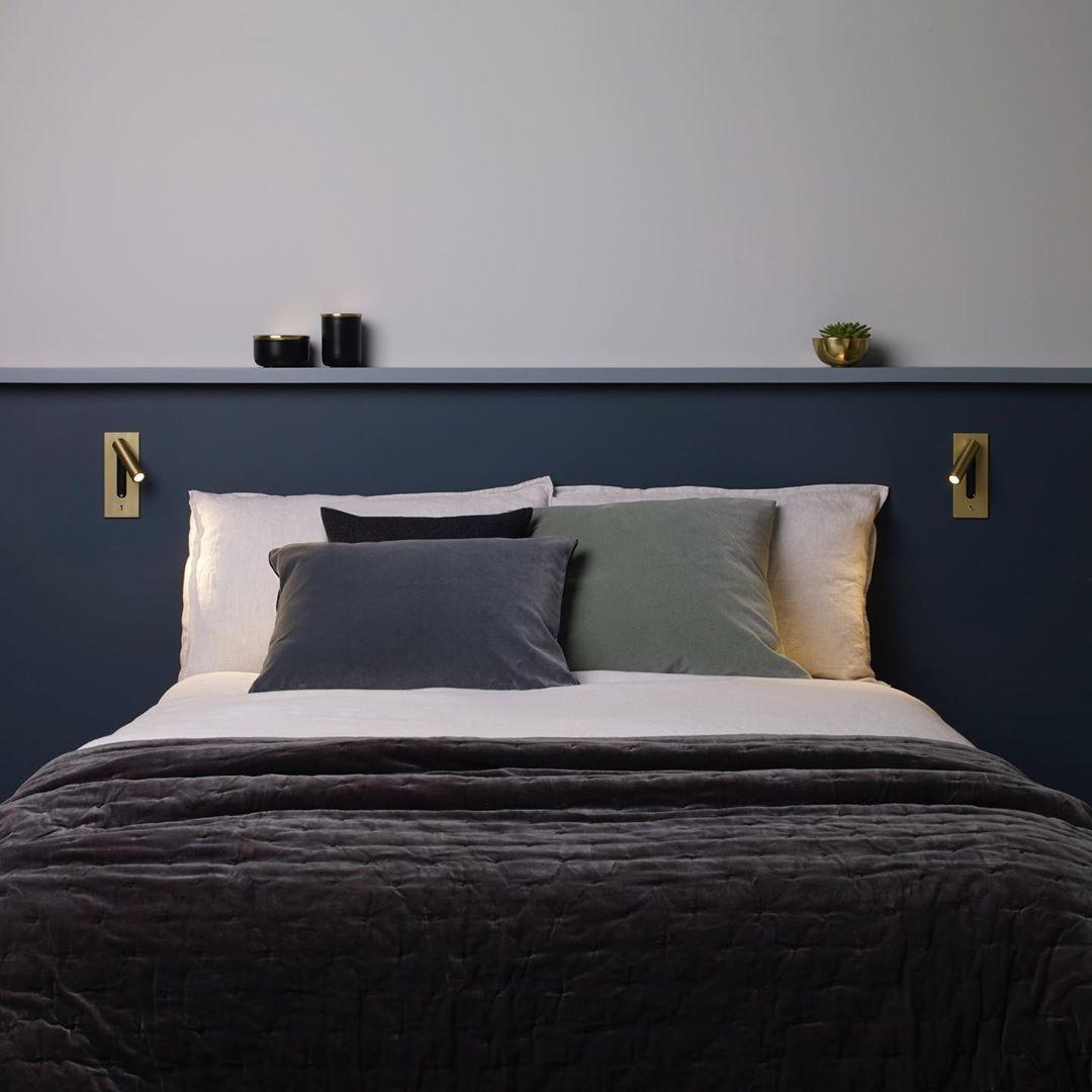 Twee gouden wandlampen aan weerszijden van een bed met donkerblauw hoofdbord, spots aan 35