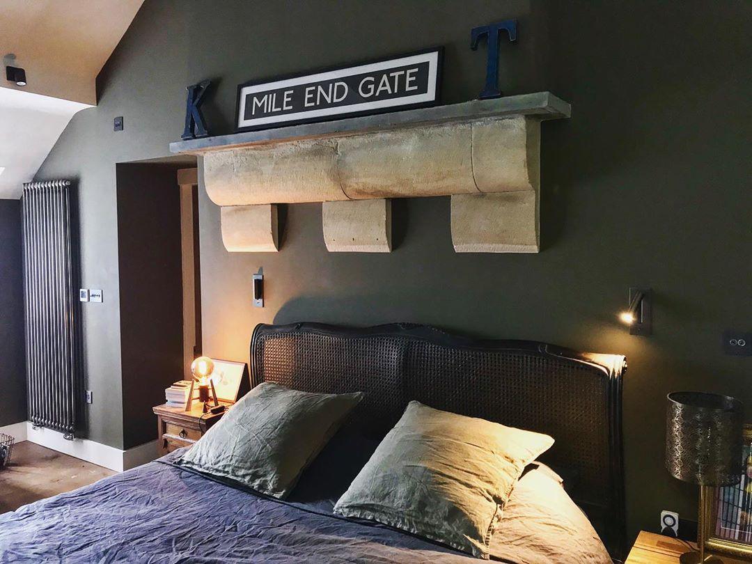 Slaapkamer met donkergroene muur en rotan hoofdbord, waarbij een wandlamp aan de rechterkant brandt 37