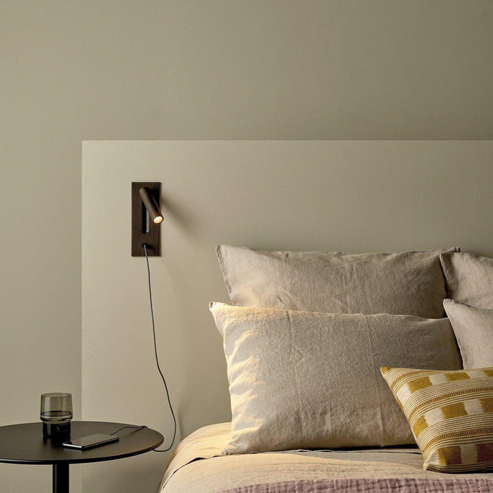 Bronskleurige wandlamp met usb-kabel naar een telefoon op een bijzettafel naast een bed 36