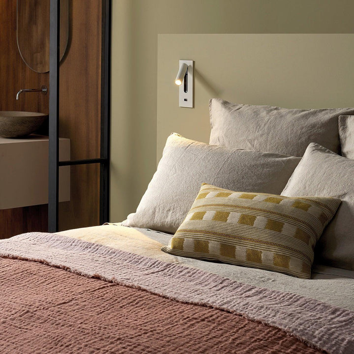 Witte wandlamp met usb-aansluiting boven een bed met linnen kussens, de spot verlicht het beddengoed 31