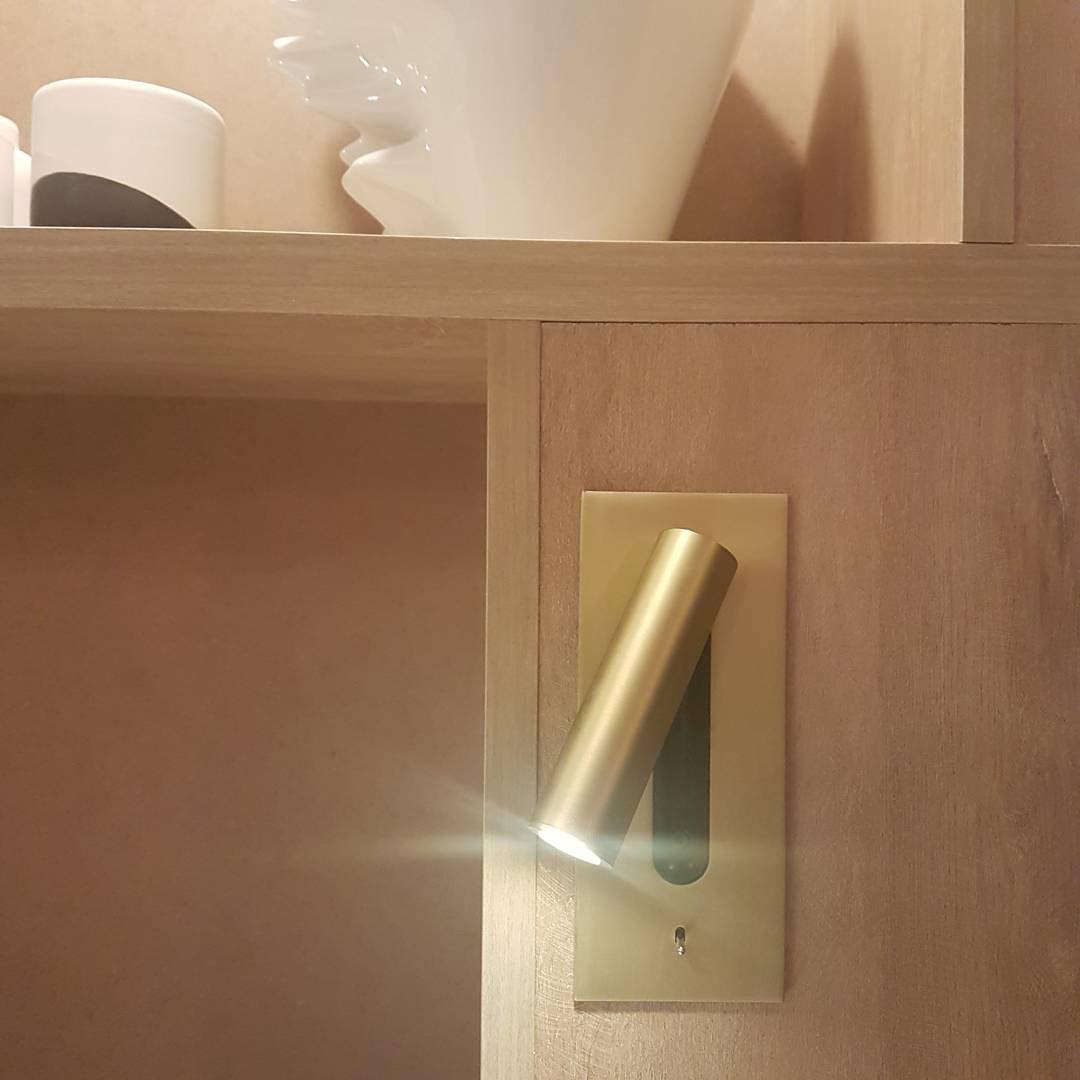 Goudkleurige wandlamp met brandende spot, ingebouwd in een houten kastwand naast open planken 32