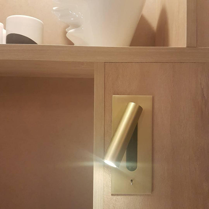 Goudkleurige wandlamp met brandende spot, ingebouwd in een houten kastwand naast open planken 32