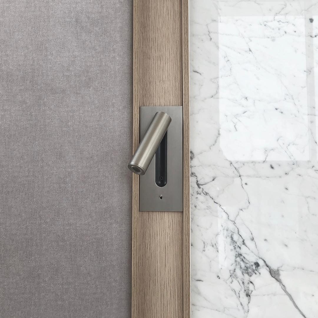 Detail van een nikkelkleurige wandlamp in een houten lijst naast wit marmer en grijze stoffen wand 33