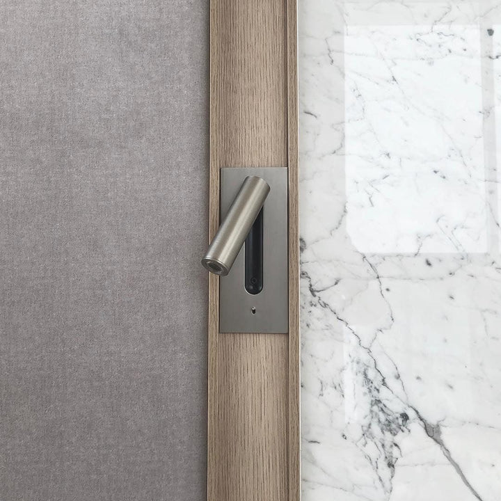 Detail van een nikkelkleurige wandlamp in een houten lijst naast wit marmer en grijze stoffen wand 33