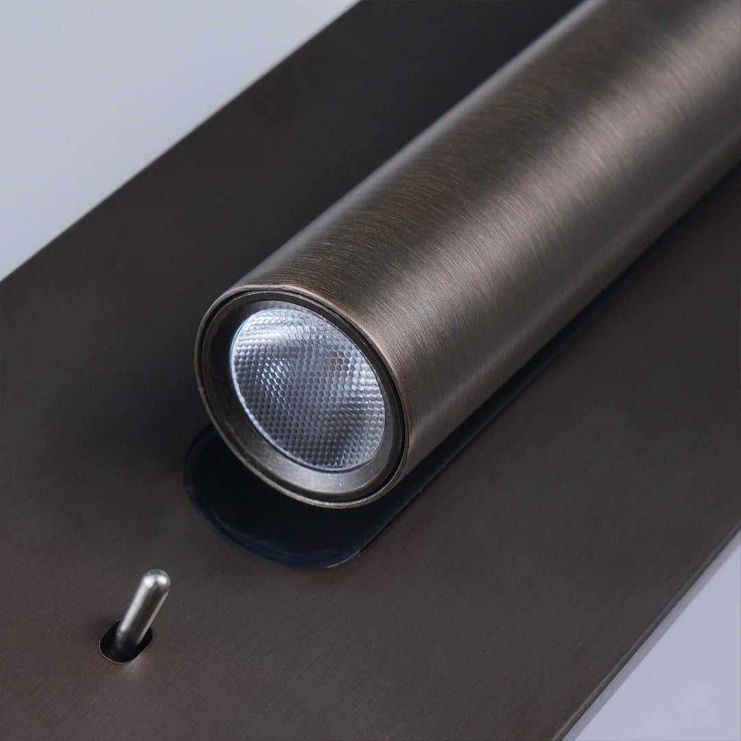 Bronskleurige wandlamp met brandende spot naar rechts en zwarte inzetstrook, tegen een witte muur 18