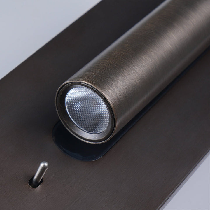 Bronskleurige wandlamp met brandende spot naar rechts en zwarte inzetstrook, tegen een witte muur 18