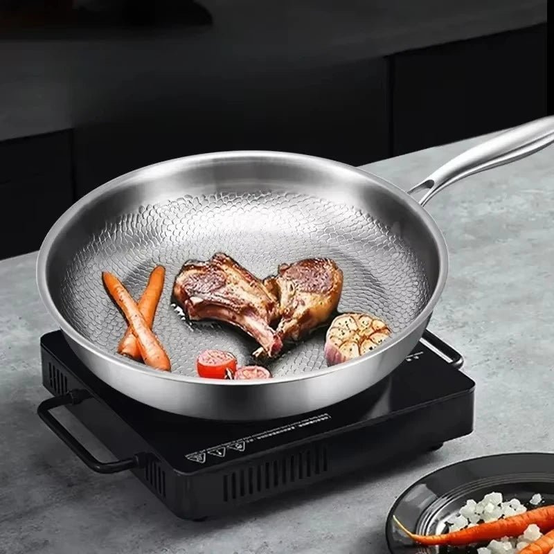 Koekenpan op een zwarte inductiekookplaat met gebakken lamsribbetjes, wortelen, knoflook en tomaat in de pan. 3