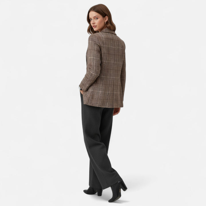 Model kijkt over haar schouder en toont de achterkant van de geruite blazer, gecombineerd met een grijze broek en zwarte laarzen. 3