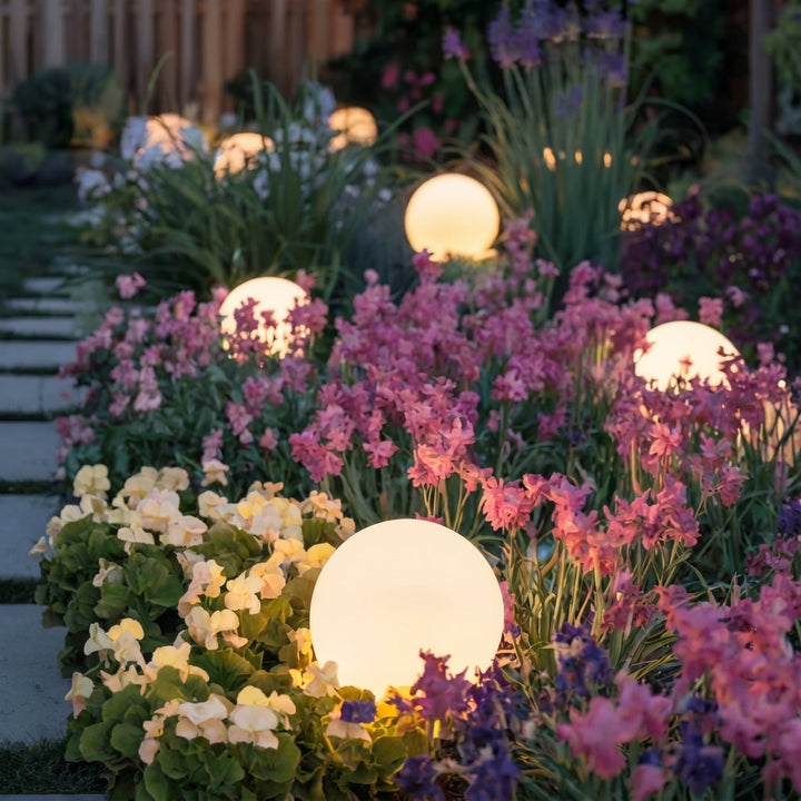 Warm gloeiende bollampen tussen roze, paarse en crèmekleurige bloemen langs een tuinpad in de schemering. 7