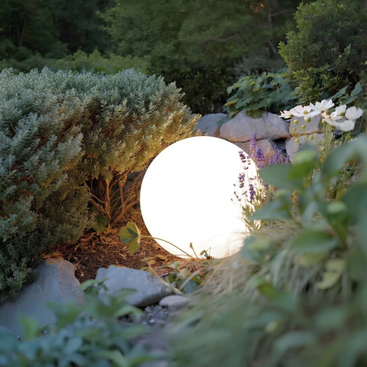 Close-up van een enkele gloeiende bollamp tussen struiken, stenen en lavendel, in de schemering gefotografeerd. 5