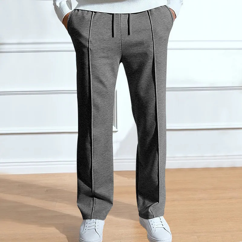Model draagt de grijze broek met trekkoord en middenvouw aan de voorkant, met witte sneakers en een witte trui. 2