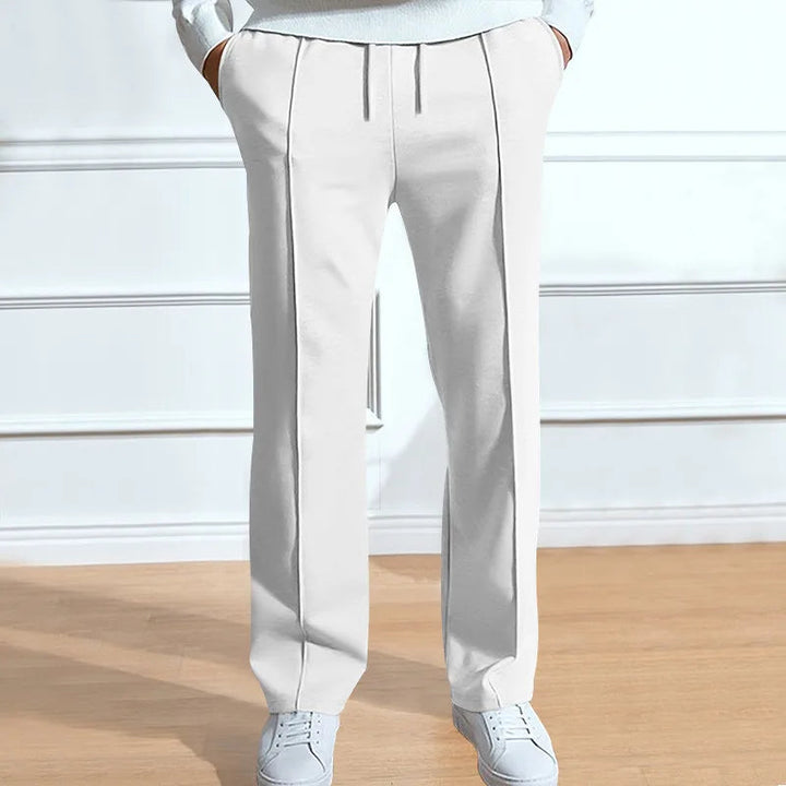 Model draagt de witte broek met trekkoord en persplooien, gecombineerd met lichte sneakers en een lichte trui. 4