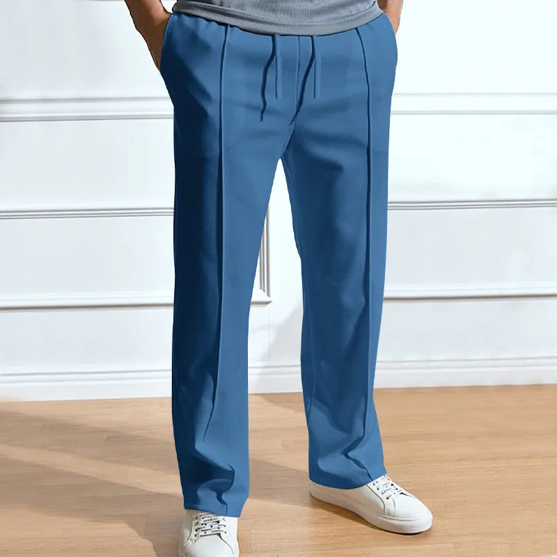 Man draagt de blauwe broek met trekkoord en persplooien, handen in de zakken, met witte sneakers en een grijs shirt. 5