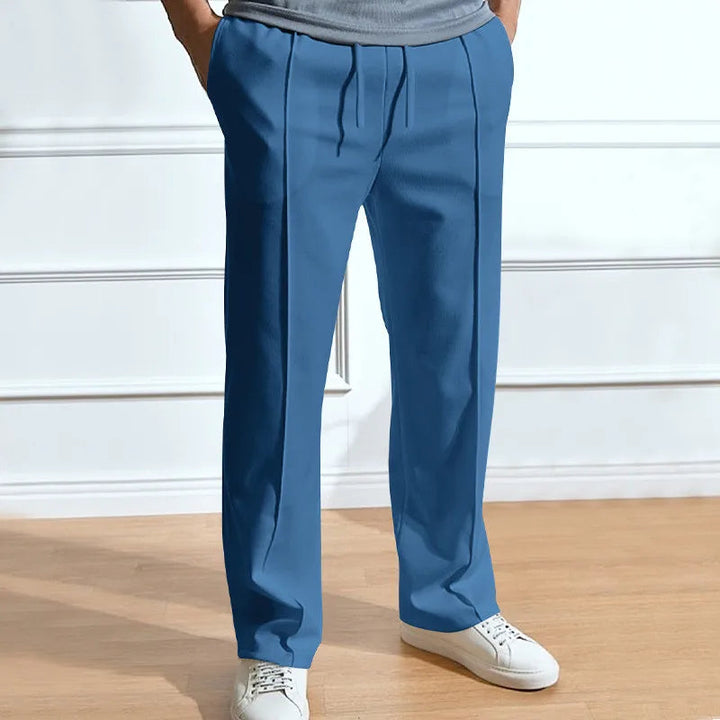 Man draagt de blauwe broek met trekkoord en persplooien, handen in de zakken, met witte sneakers en een grijs shirt. 5