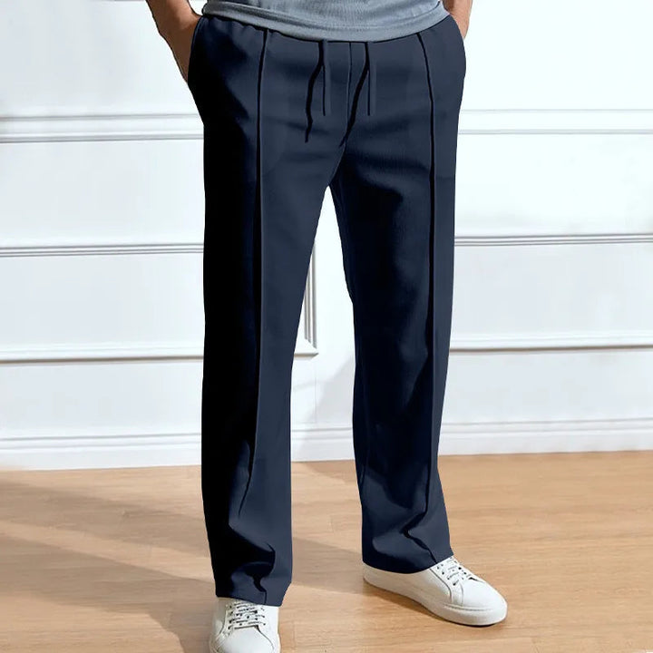 Man draagt de marineblauwe broek met trekkoord, persplooien en handen in de zakken, gecombineerd met wit sneakers en grijs shirt. 1