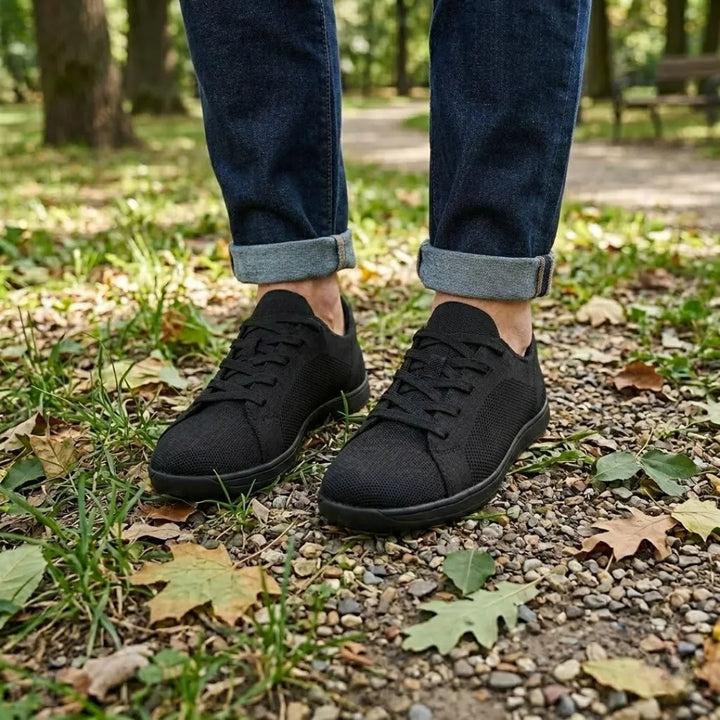 Zwarte sneakers gedragen met een donkerblauwe spijkerbroek met omgeslagen pijpen, op een grindpad met gevallen bladeren. 11