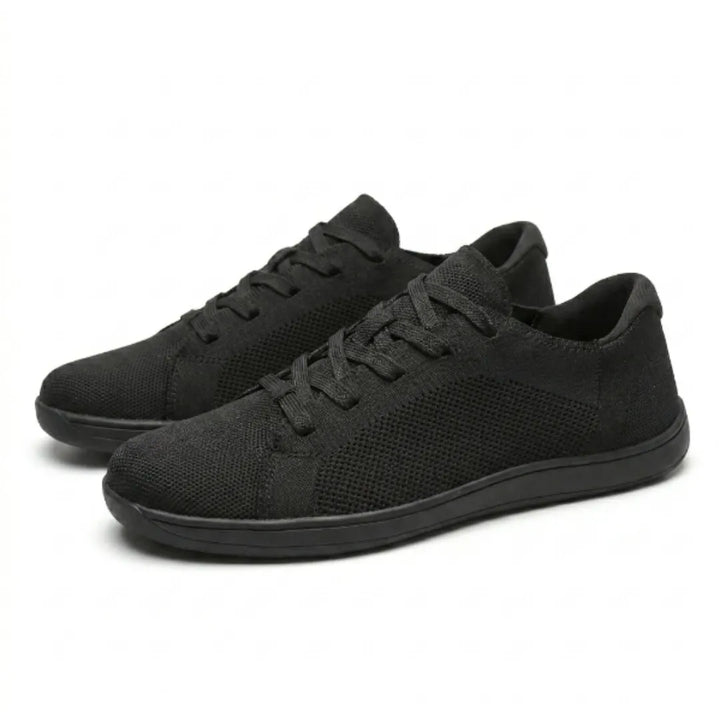 Twee zwarte mesh sneakers schuin van voren op een witte achtergrond, met veters en een zwarte zool. 16