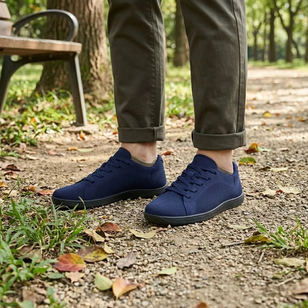 Marineblauwe sneakers met zwarte zool gedragen met een olijfgroene broek, op een grindpad naast een parkbankje. 20