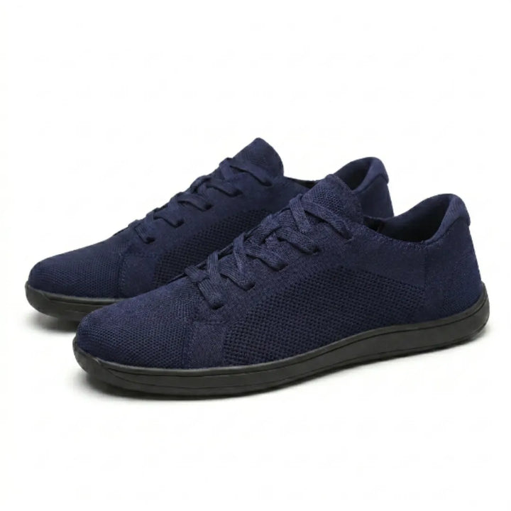 Paar marineblauwe gebreide sneakers met zwarte zool en veters, schuin van opzij gefotografeerd op een witte achtergrond. 25