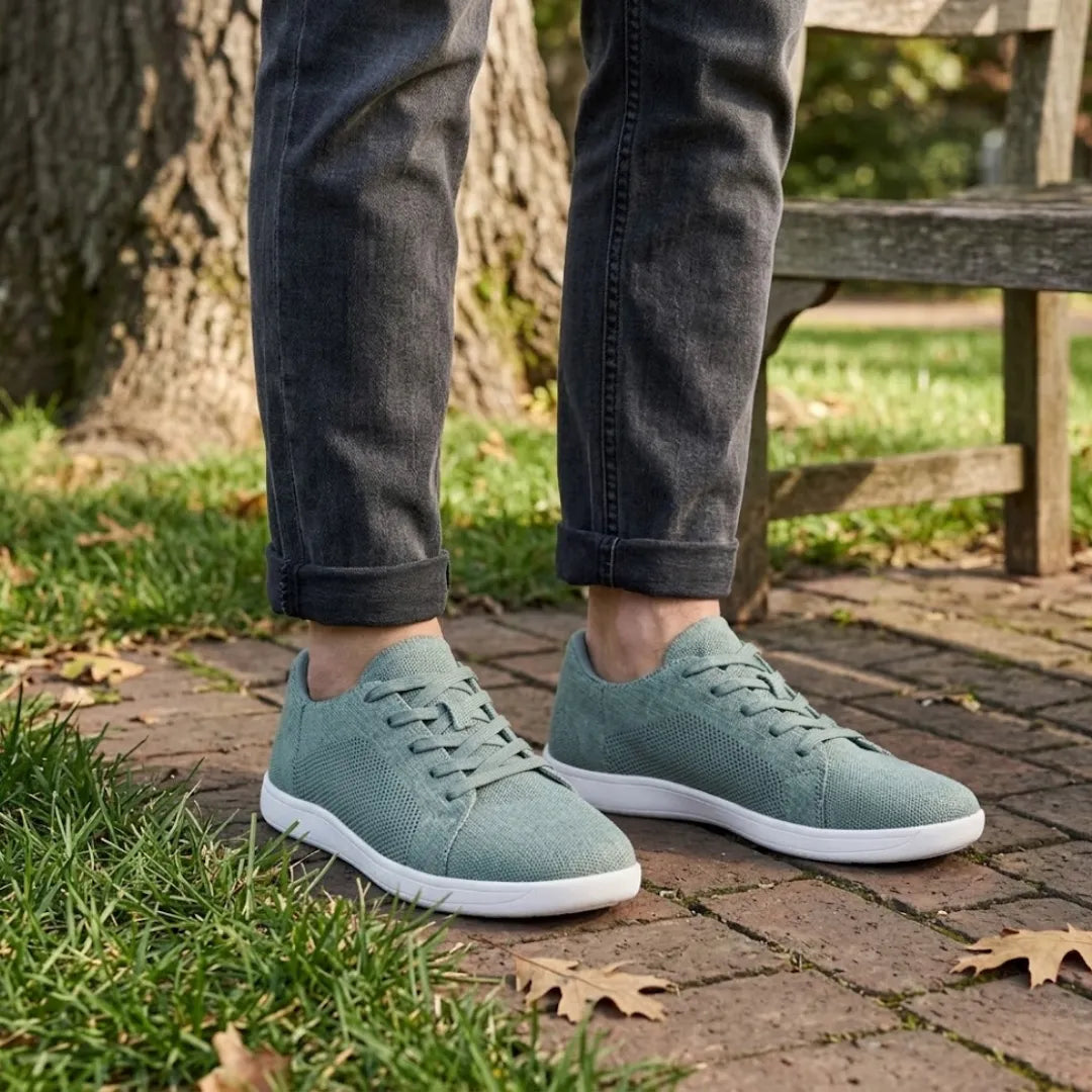Persoon draagt de saliegroene sneakers met witte zool en een grijze jeans met omgeslagen pijpen op een stenen pad bij een bankje. 29