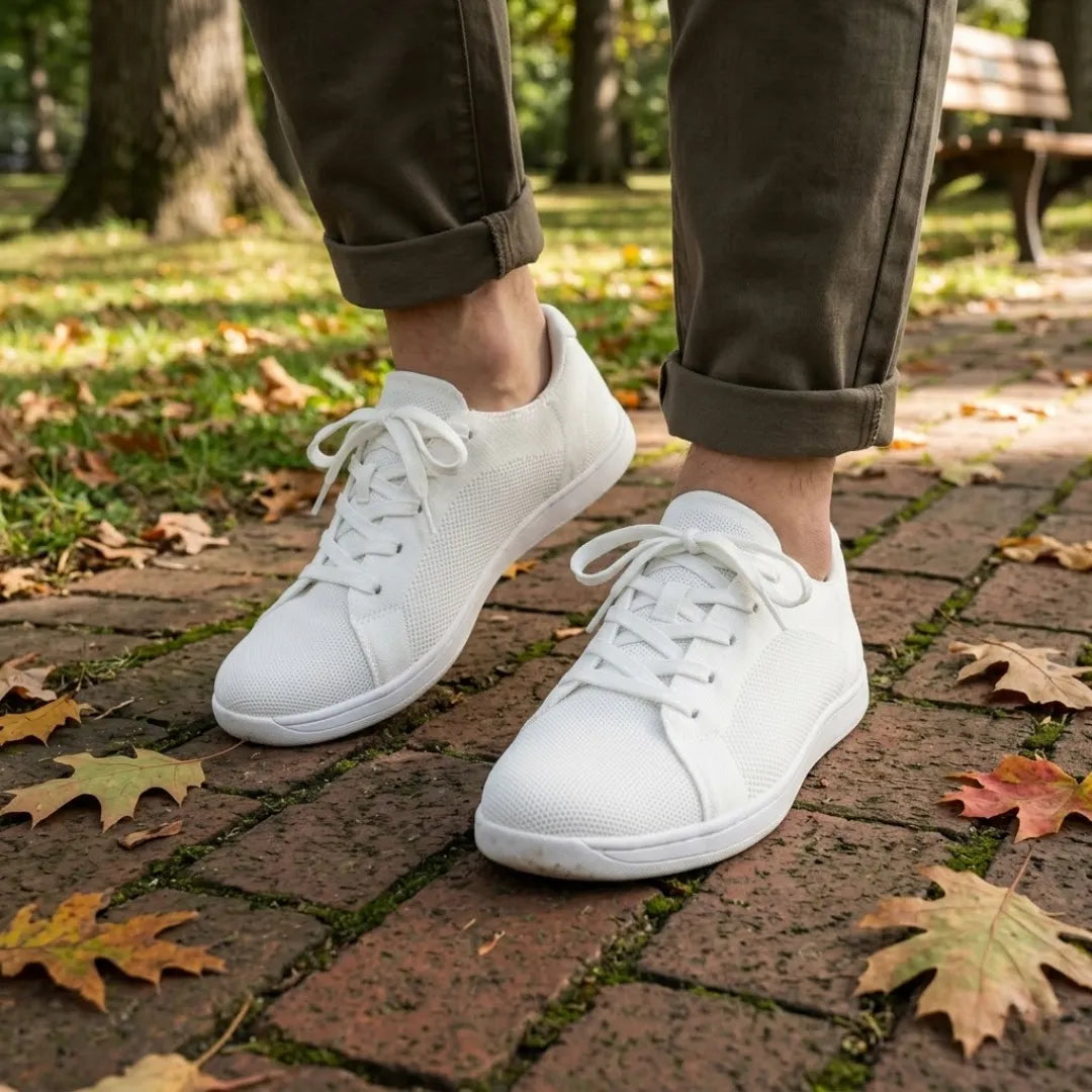 Persoon draagt de witte sneakers met een olijfgroene broek met omgeslagen pijpen op een stenen pad met herfstbladeren. 38