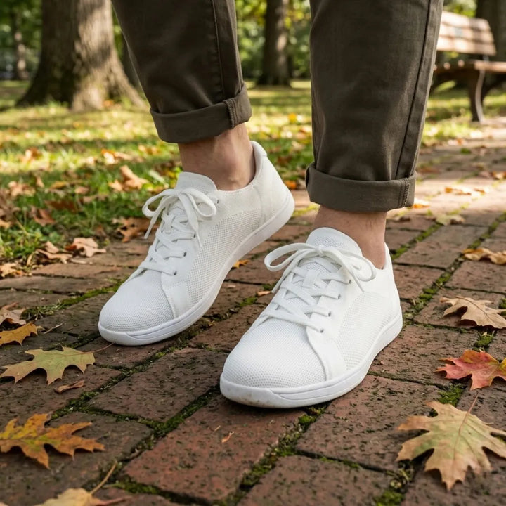 Persoon draagt de witte sneakers met een olijfgroene broek met omgeslagen pijpen op een stenen pad met herfstbladeren. 38