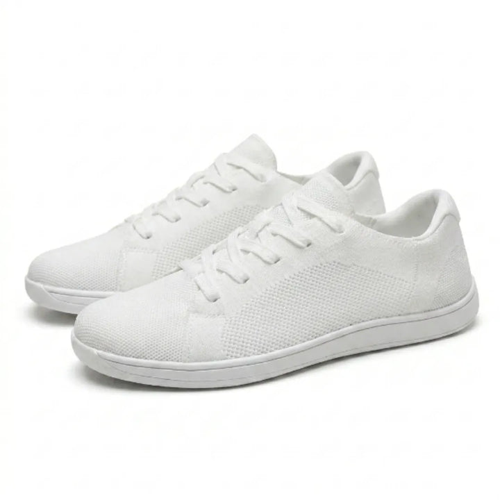 Paar witte gebreide barefoot-sneakers met veters en dunne witte zool, schuin van opzij gefotografeerd op een lichte achtergrond. 43