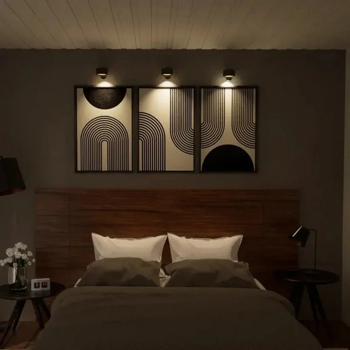 Drie zwarte wandlampen verlichten elk een ingelijst schilderij boven een bed in een slaapkamer 10