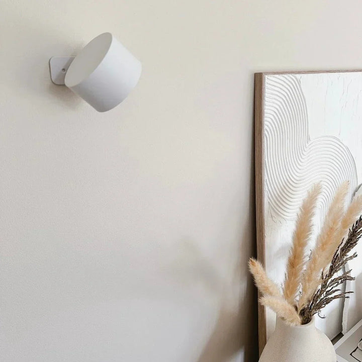 Witte wandlamp uitgeschakeld aan een lichte muur naast een lijst en een vaas met pampasgras 16