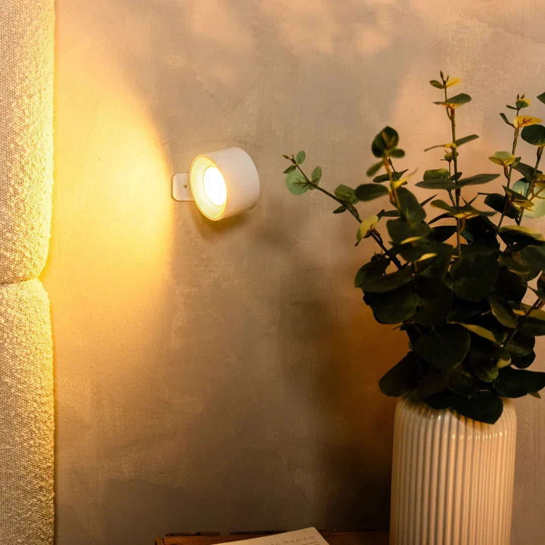Witte wandlamp aan een betonlook muur naast een plant in een geribbelde vaas 6