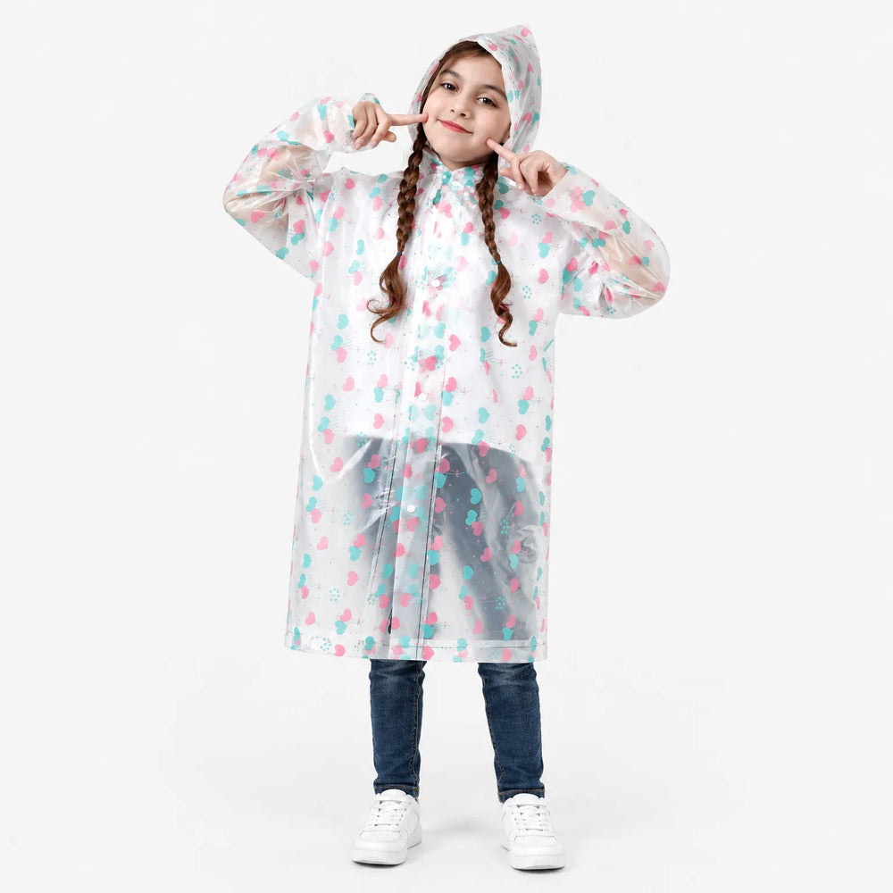 Lachend meisje met vlechten poseert in de doorzichtige regenjas met hartjesprint, over spijkerbroek en witte sneakers, tegen een witte achtergrond. 2