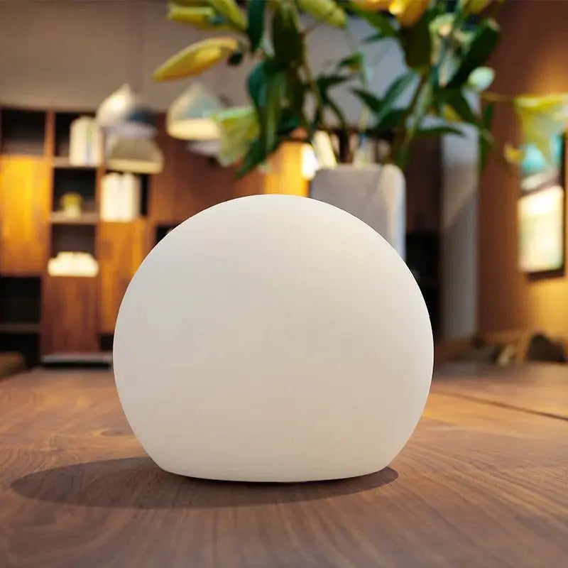 Uitgeschakelde witte ledbol op een houten tafel in een woonkamer met planten en een open kast op de achtergrond. 3