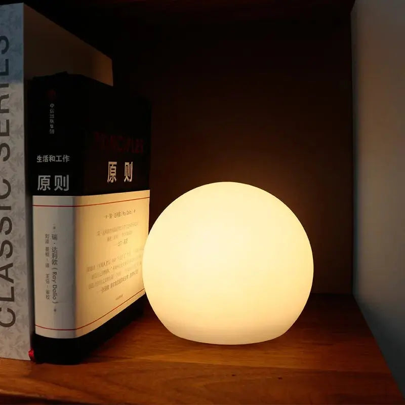 Warm oplichtende ledbol op een boekenplank, tegen een staande stapel boeken aan geplaatst. 4