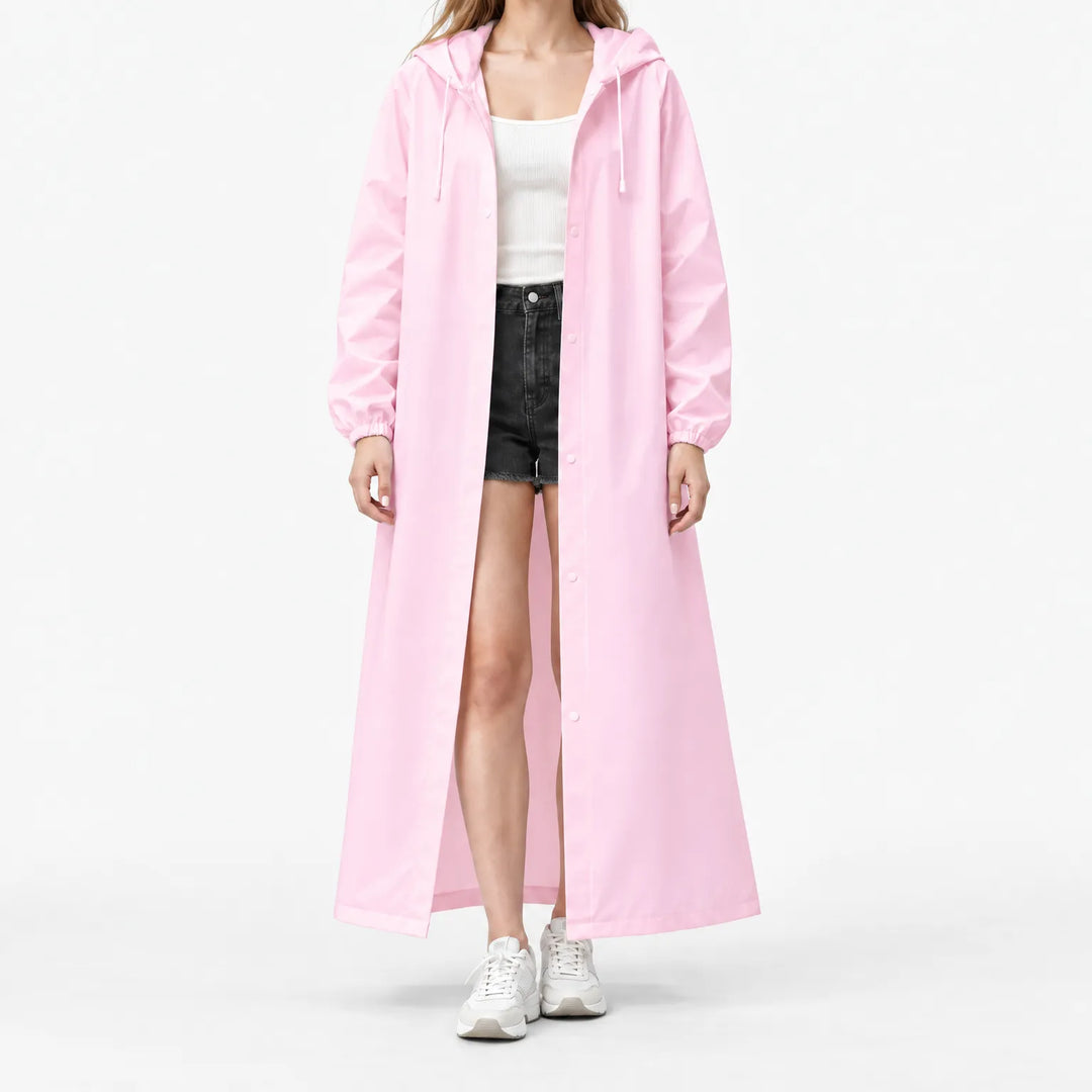 Model op witte achtergrond draagt de lange roze regenjas open, met capuchon, drukknopen en elastische manchetten, over wit topje en korte broek. 7