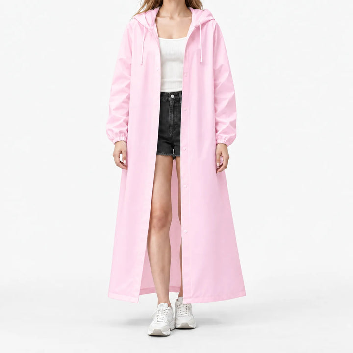 Model op witte achtergrond draagt de lange roze regenjas open, met capuchon, drukknopen en elastische manchetten, over wit topje en korte broek. 7