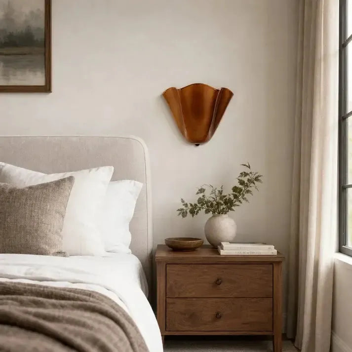 Uitgeschakelde wandlamp in koperbruin glas boven een houten nachtkastje in een slaapkamer met linnen gordijn en vaas. 3