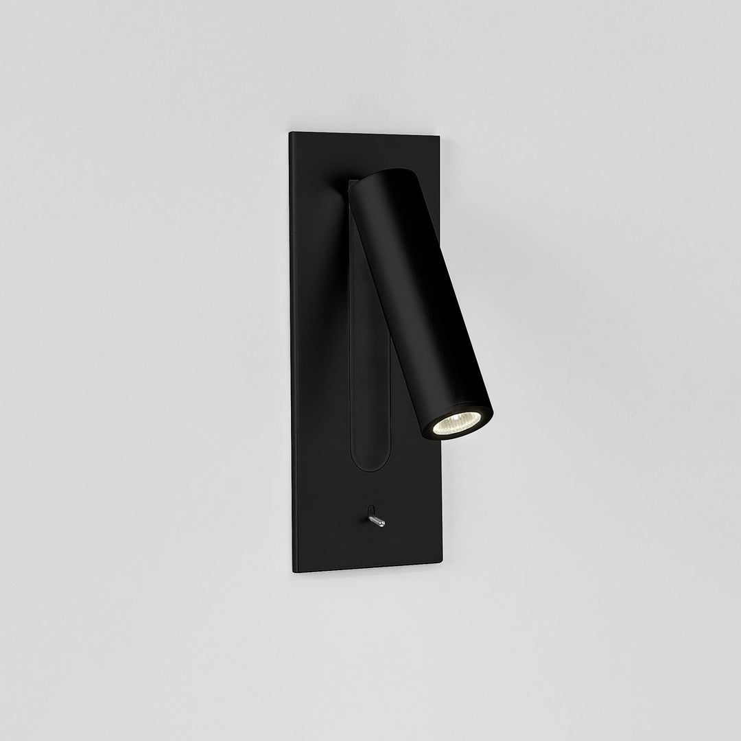 Witte wandlamp met zwarte inzetstrook en brandende spot naar rechts, schakelaar onderaan, op grijze achtergrond 12