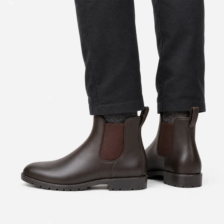 Zijaanzicht van bruine enkellaarzen met bruin elastiek en profielzool, gedragen onder een donkere broek met grijze sokken. 4
