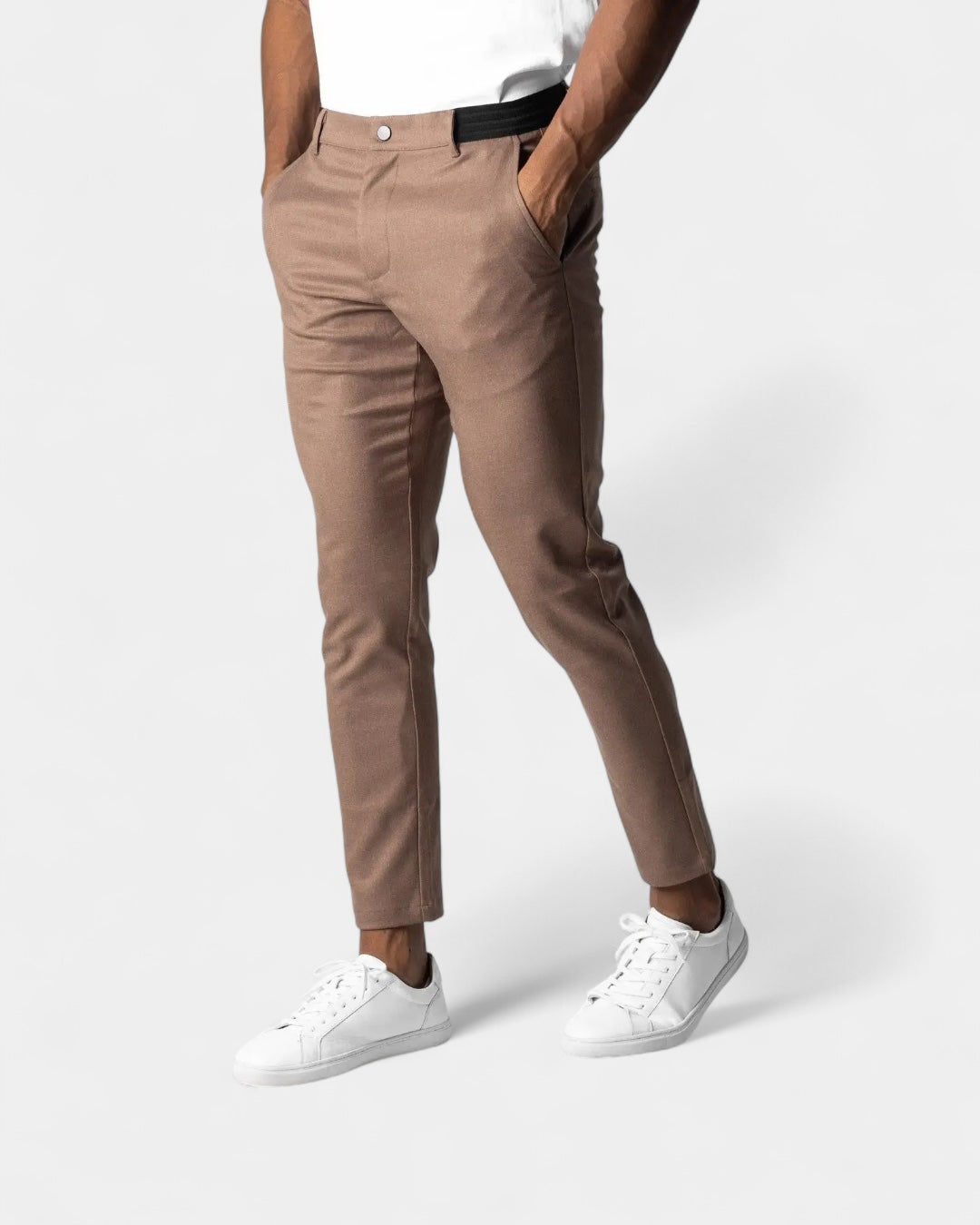 Model draagt de bruine broek met taps toelopende pijpen en witte sneakers, hand in de zak 5