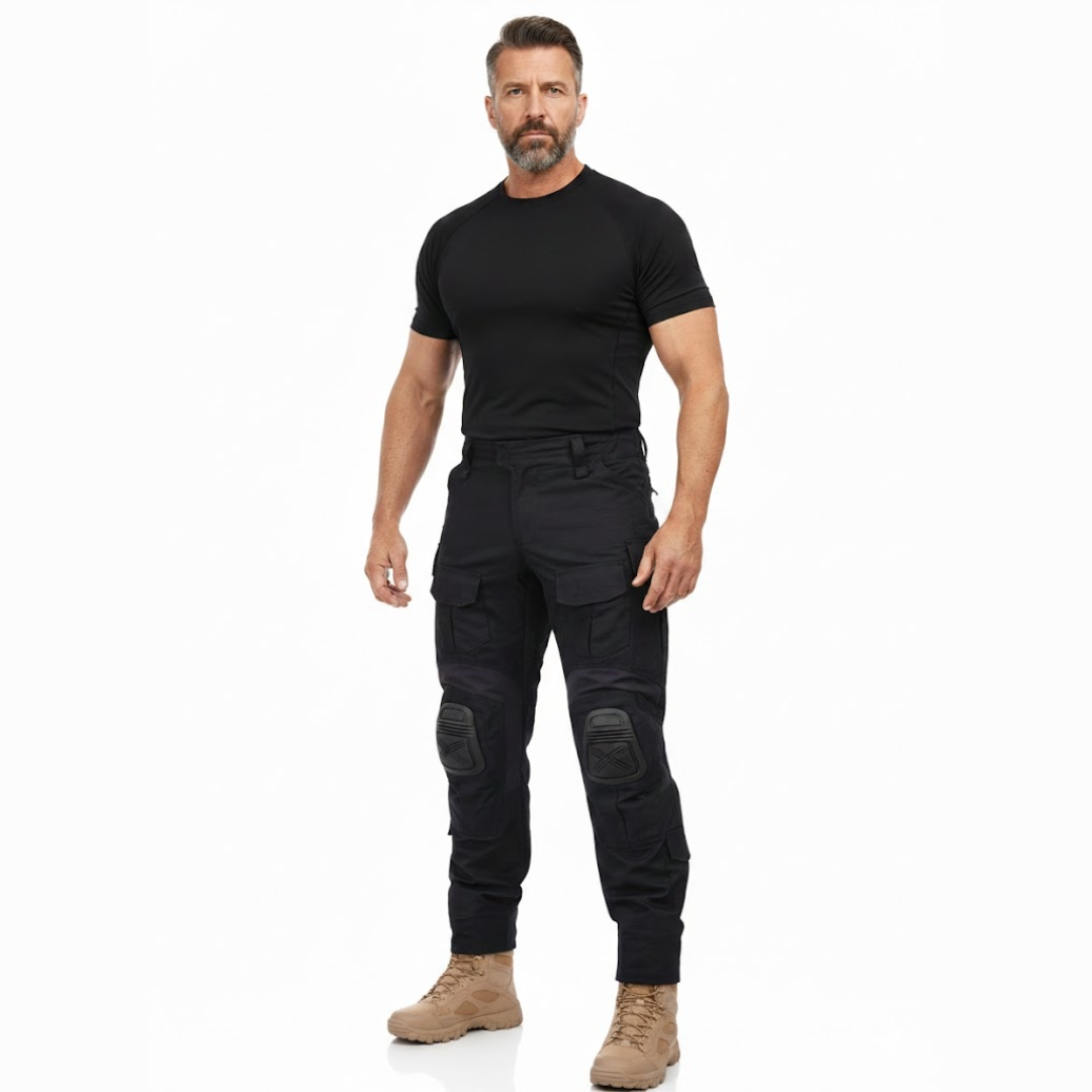 Man met baard staat in volledige lengte in zwart shirt, de zwarte cargobroek met kniekappen en beige laarzen. 7