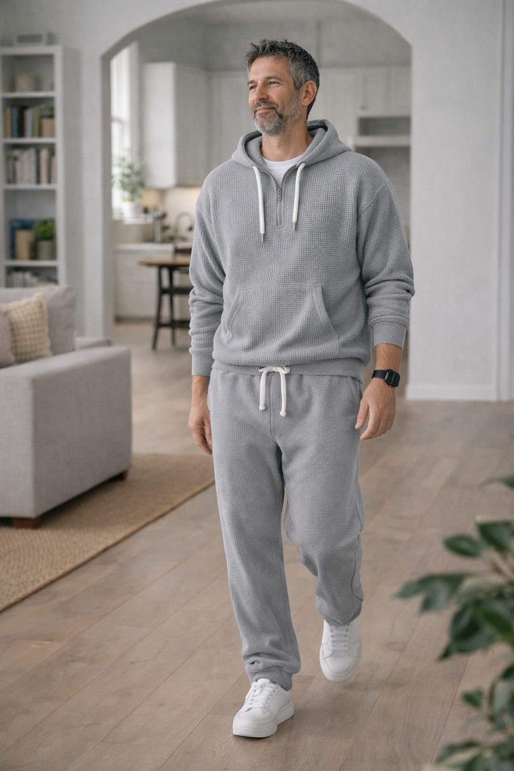 Man draagt de grijze set met halve rits en joggingbroek terwijl hij door een lichte woonkamer loopt. 2