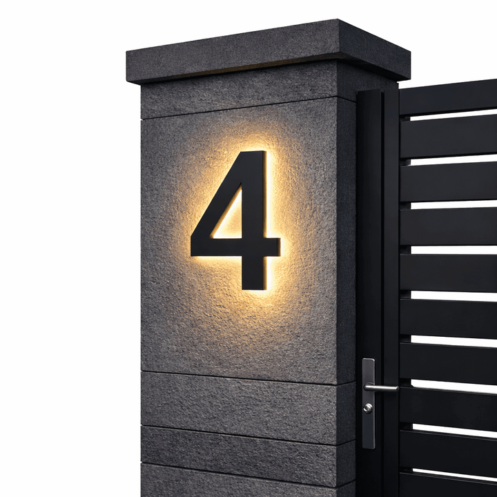 Zwart huisnummer 4 met warme achtergrondverlichting op een grijze stenen poortpilaar naast een zwarte poort met deurkruk. 10
