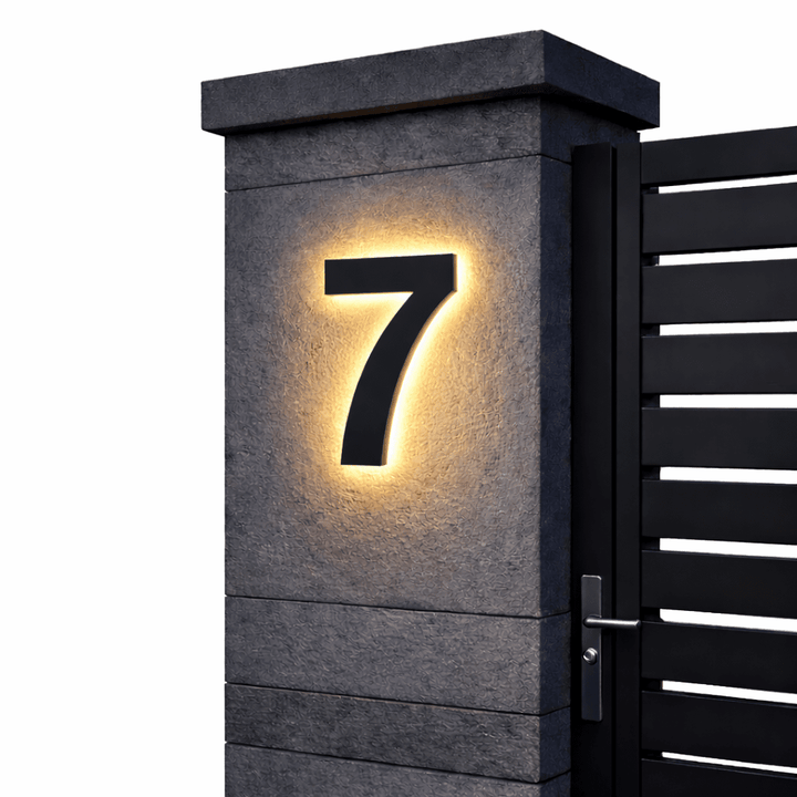 Zwart huisnummer 7 met zachte verlichting langs de randen op een grijze stenen poortpilaar naast een zwarte poort. 13