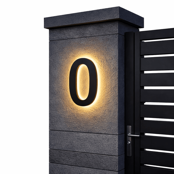 Zwart huisnummer 0 met warm achtergrondlicht op een grijze stenen poortpilaar naast een zwarte lamellenpoort. 6