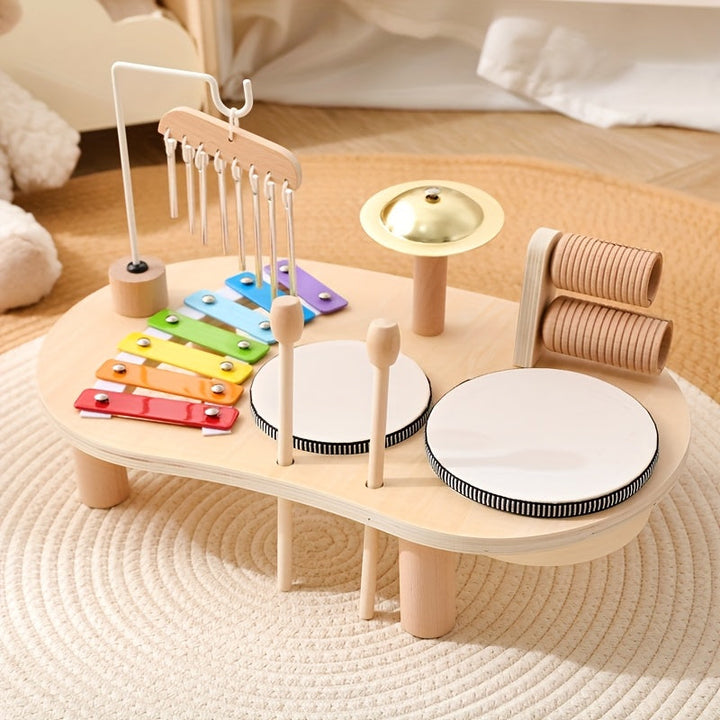 Houten muziektafel met regenboogxylofoon, windgong, bekken, twee trommels en houten rasp op een crèmekleurig rond kleed. 1