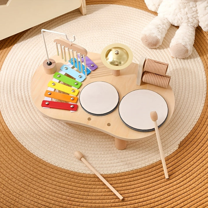 Bovenaanzicht van de muziektafel op een rond gevlochten kleed, met twee houten stokjes los ervoor en een knuffel in de hoek. 8