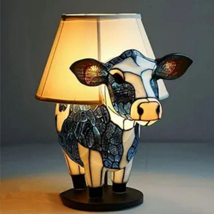 Koe in blauw-wit glasmozaïek die als voet dient van een tafellamp met een crèmekleurige stoffen kap en warme verlichting. 12